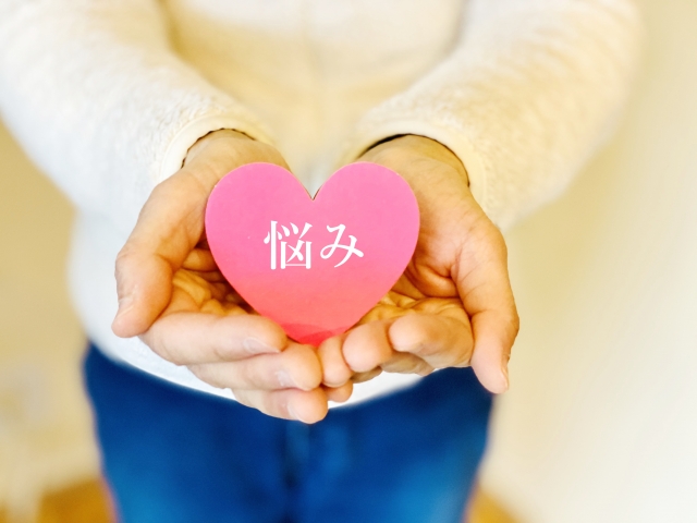 手に「悩み」と書かれたハートを持つ写真。職場で軽く見られる感覚や人間関係の悩み、心の距離を整えるヒントをイメージ。