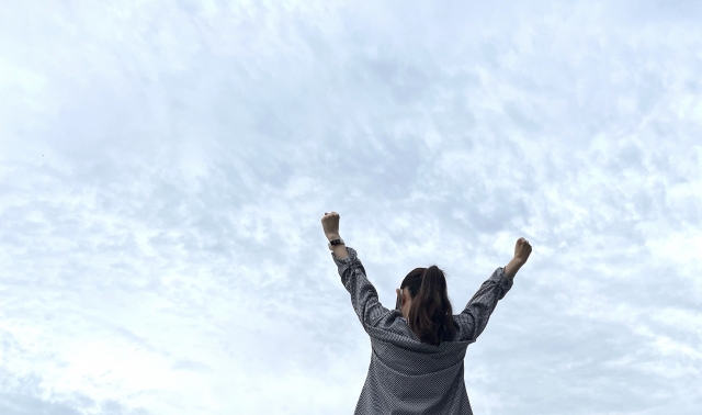 外で手を広げて空を見上げる人。職場の違和感やモヤモヤを整理して、心の距離を整えるイメージ。